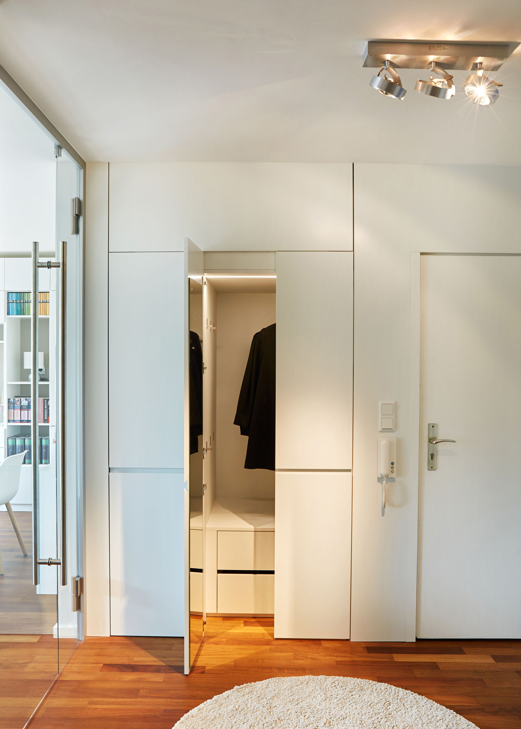 Foto: Moderner, heller Eingangsbereich eines Wohnraums mit weißem Garderoben Einbauschrank, warmem Parkettboden und Glastür zum Wohnbereich.