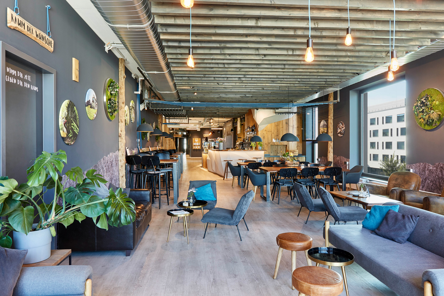 Foto: Modern gestalteter Aufenthaltsbereich mit Lounge-Möbeln, Holzdecke, dunklen Wänden, industriellen Gestaltungselementen und großzügiger Verglasung in wohnlicher Atmosphäre.