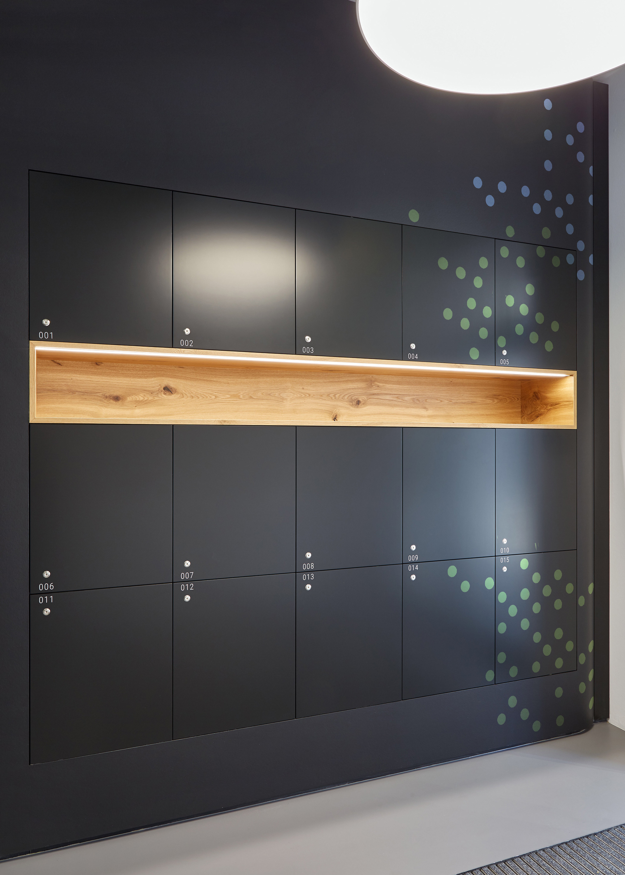 Foto: Moderner schwarzer Einbauschrank mit Schließfächern, Eichenholz Einsatz und grün-blauer Folierung in Punktmuster.