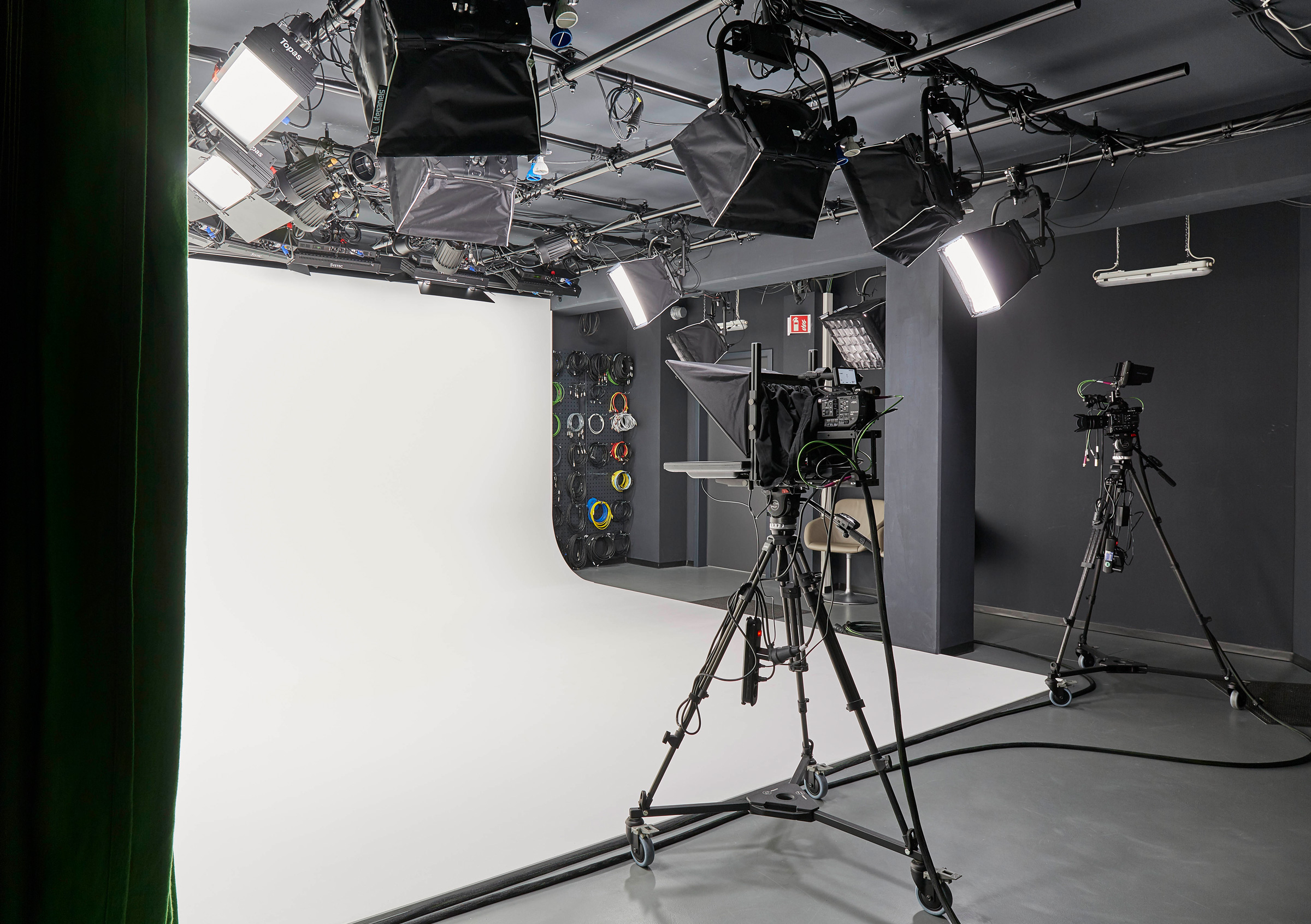 Foto: Modern, technisch gut ausgestattetes Filmstudio mit Schwarzen Wänden, Kamera, Scheinwerfern und weißem Backdrop.