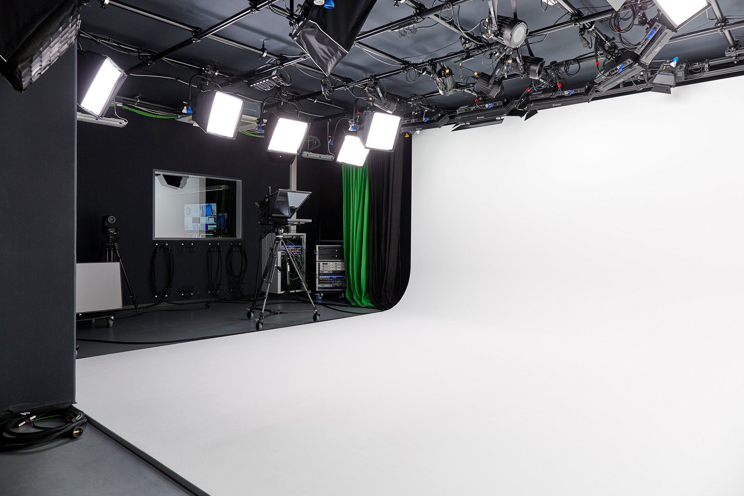 Foto: Modern, technisch gut ausgestattetes Filmstudio mit Schwarzen Wänden, Kamera, Scheinwerfern und weißem Backdrop.