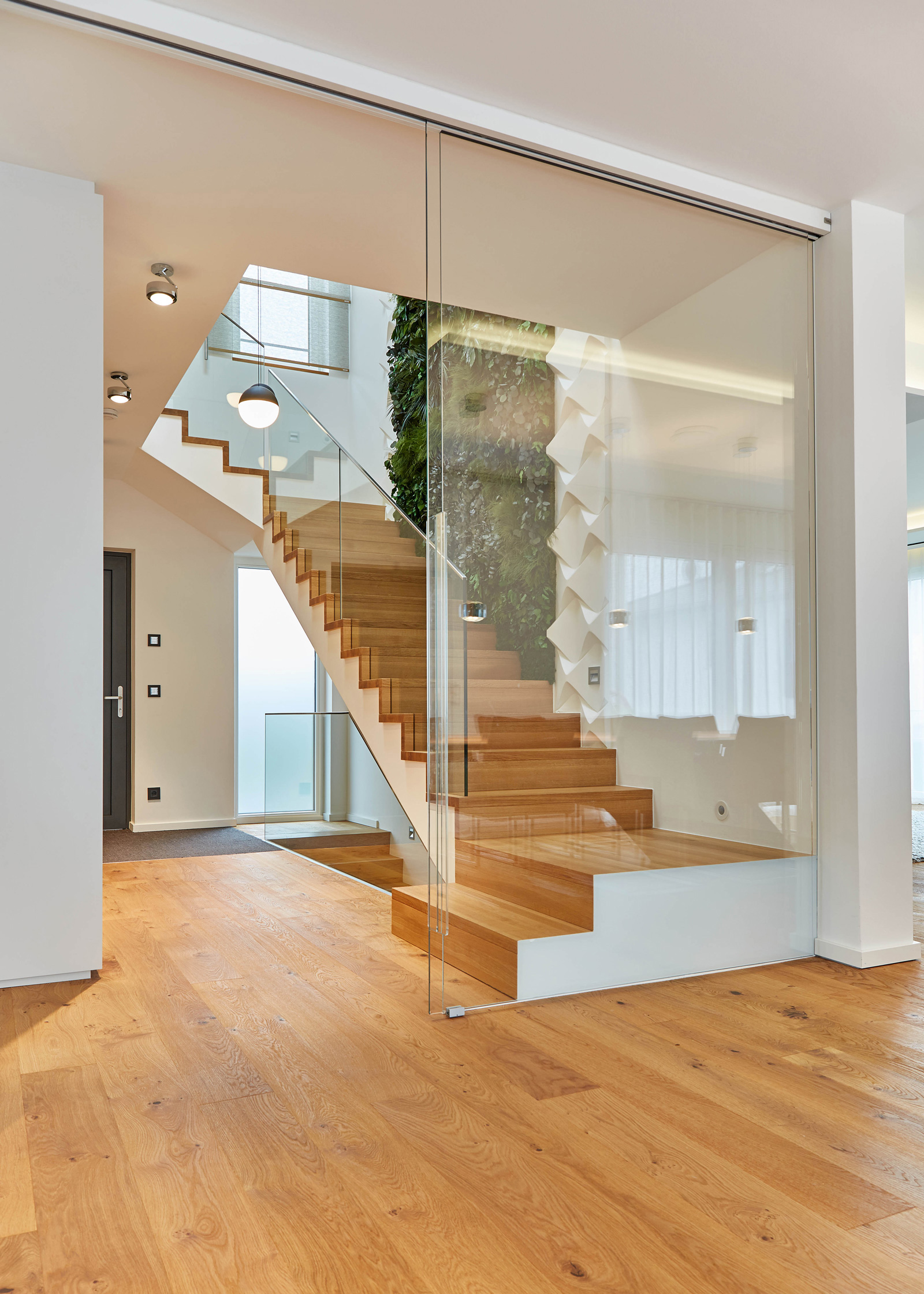 Foto: Moderner Eingangsbereich mit offener, repräsentativer Holz Treppe, abgetrennt vom Wohnbereich durch raumhohe Glasschiebetüren.