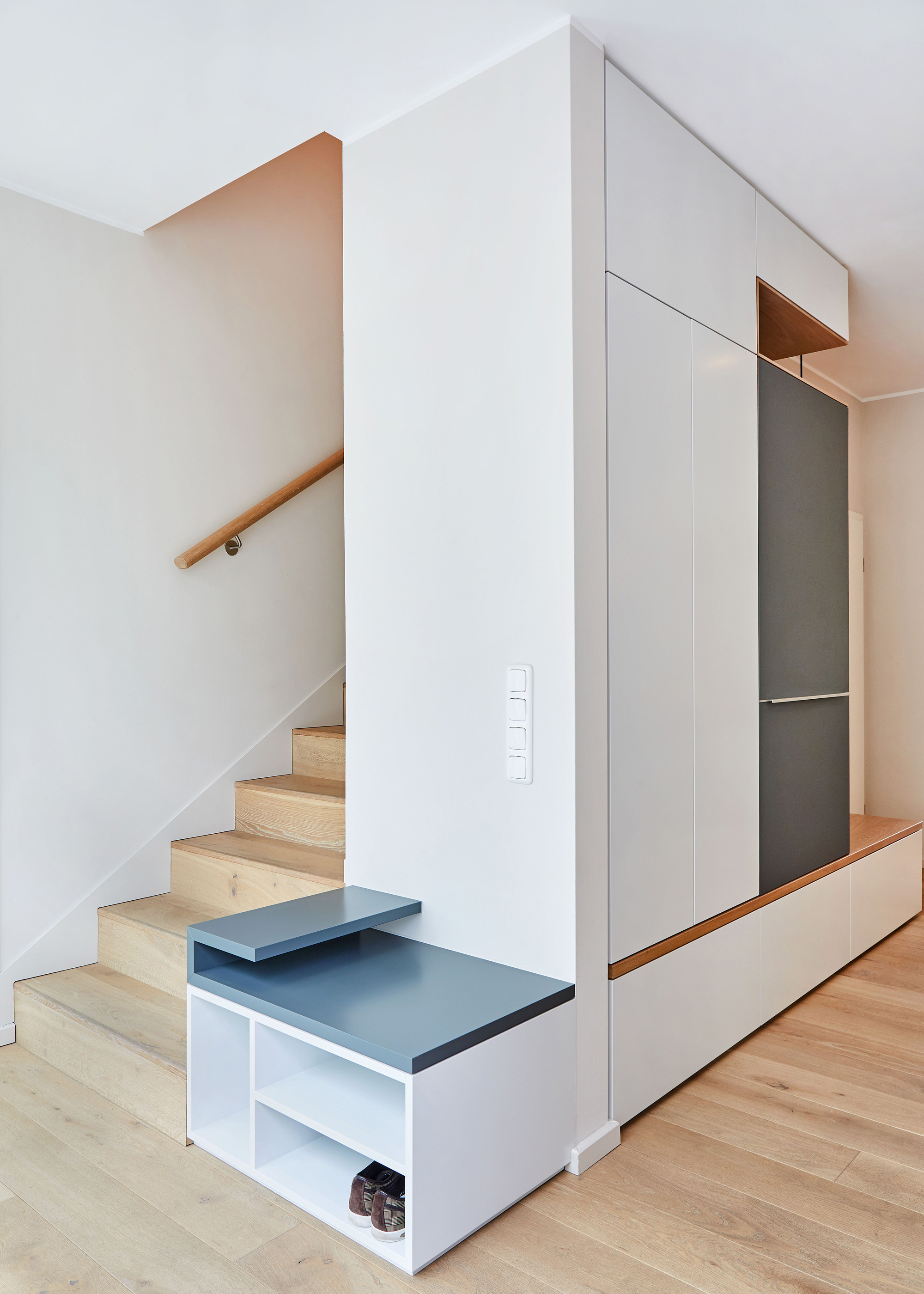 Foto: Moderner Eingangsbereich mit Treppe und raumbildendem Einbaumöbel mit Stauraum, integrierter Sitzbank und Garderobe.