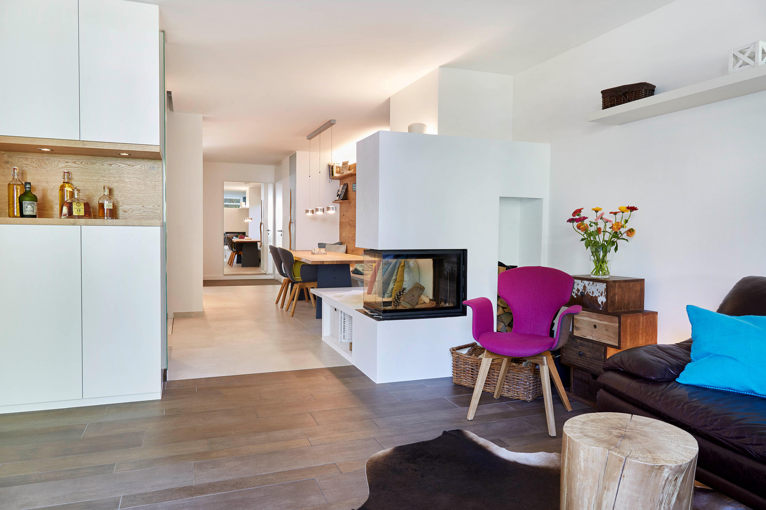 Foto: Offen gestalteter Wohn- und Essbereich mit modernem Kamin, violettem Sessel, dunklem Ledersofa und heller Küche in minimalistischem Design.