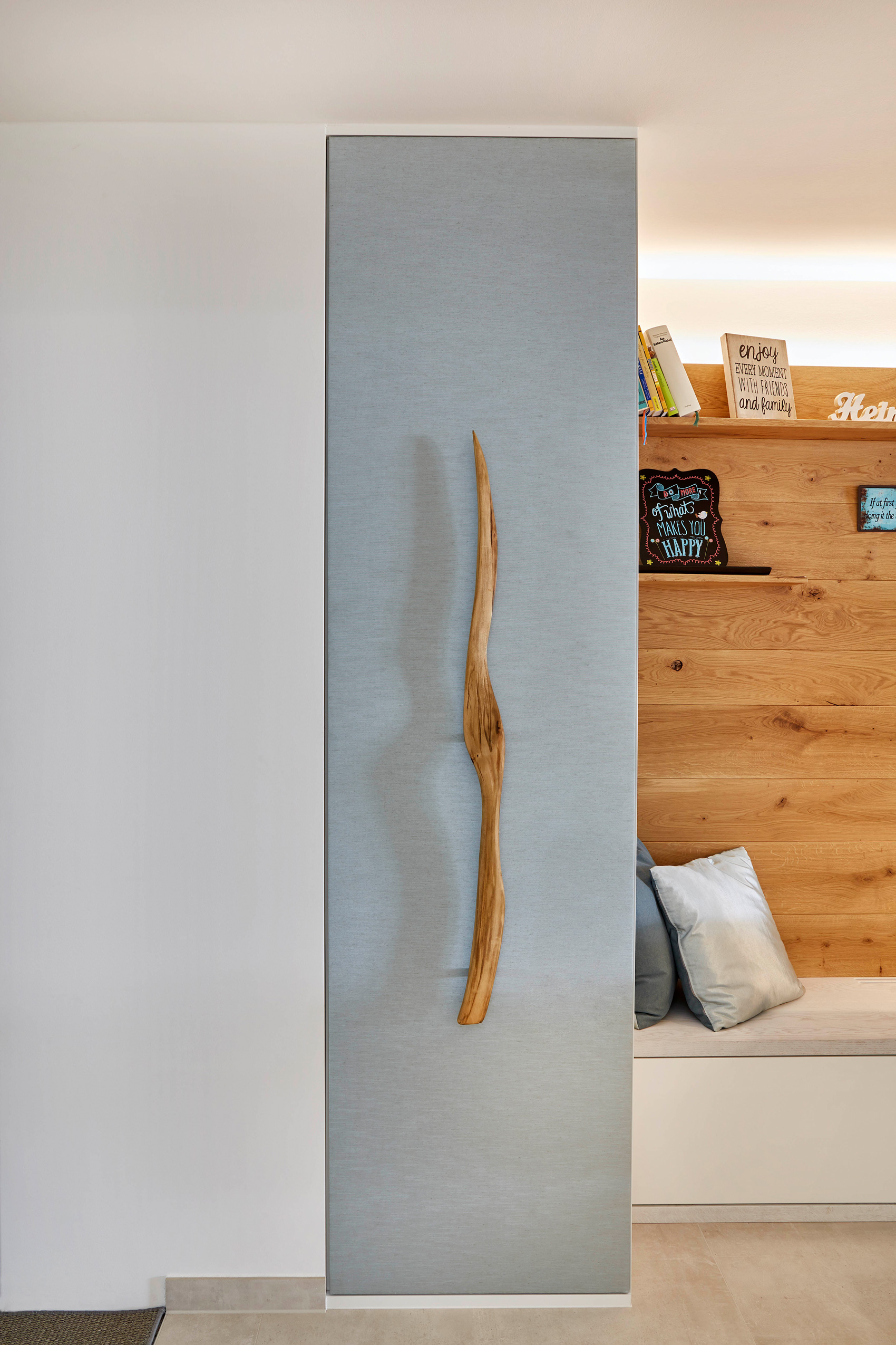Foto: Detailaufnahme, raumhoher, grauer Einbauschrank mit Treibholz Ast als Griff, neben Sitzbank mit Holz Wandvertäfelung. 