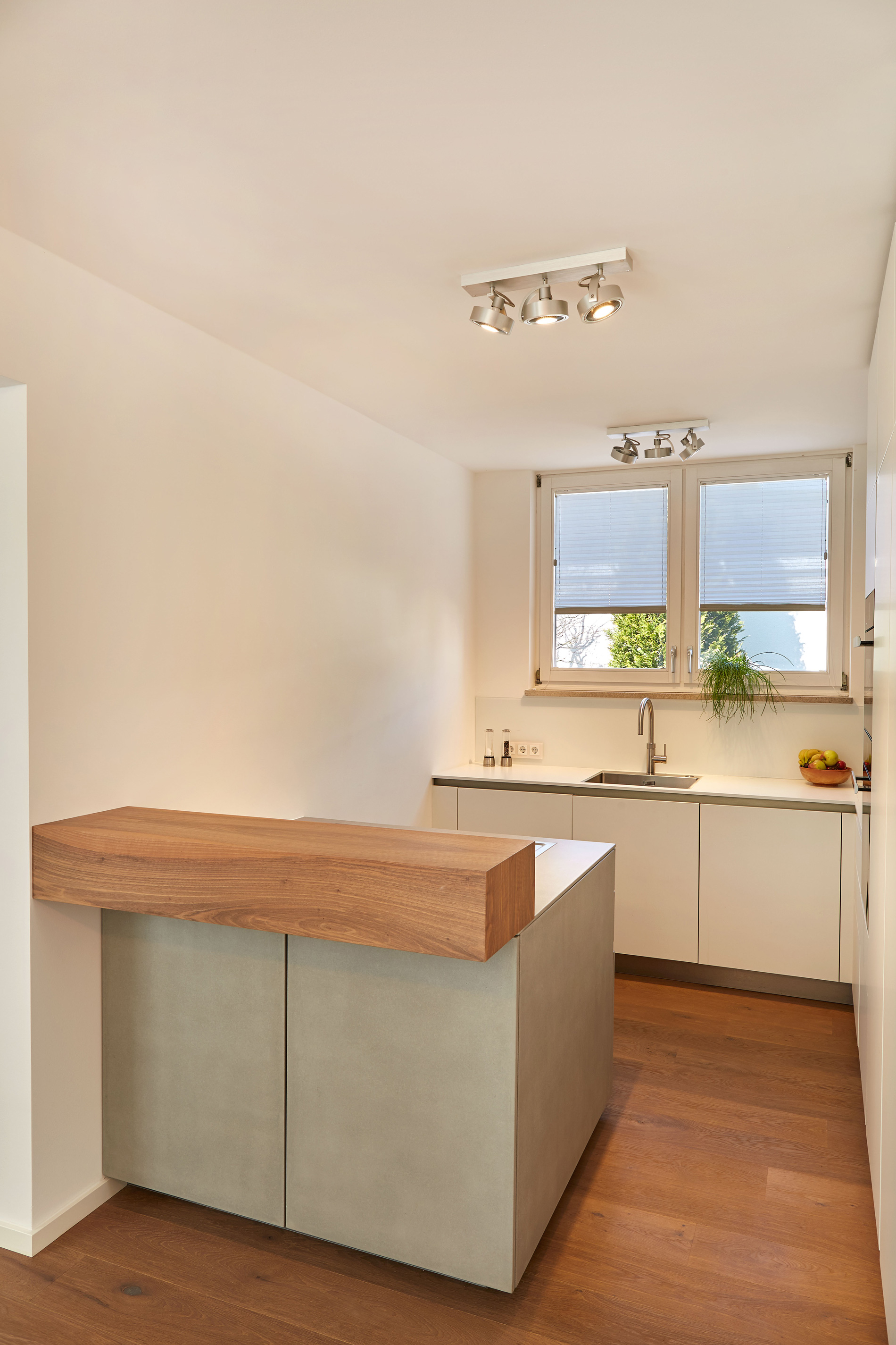 Foto: Helle, moderne, kompakte Küche mit kleiner, grauer Kücheninsel mit Holztresen und minimalistischer, weißer Küchenzeile unterm Fenster.