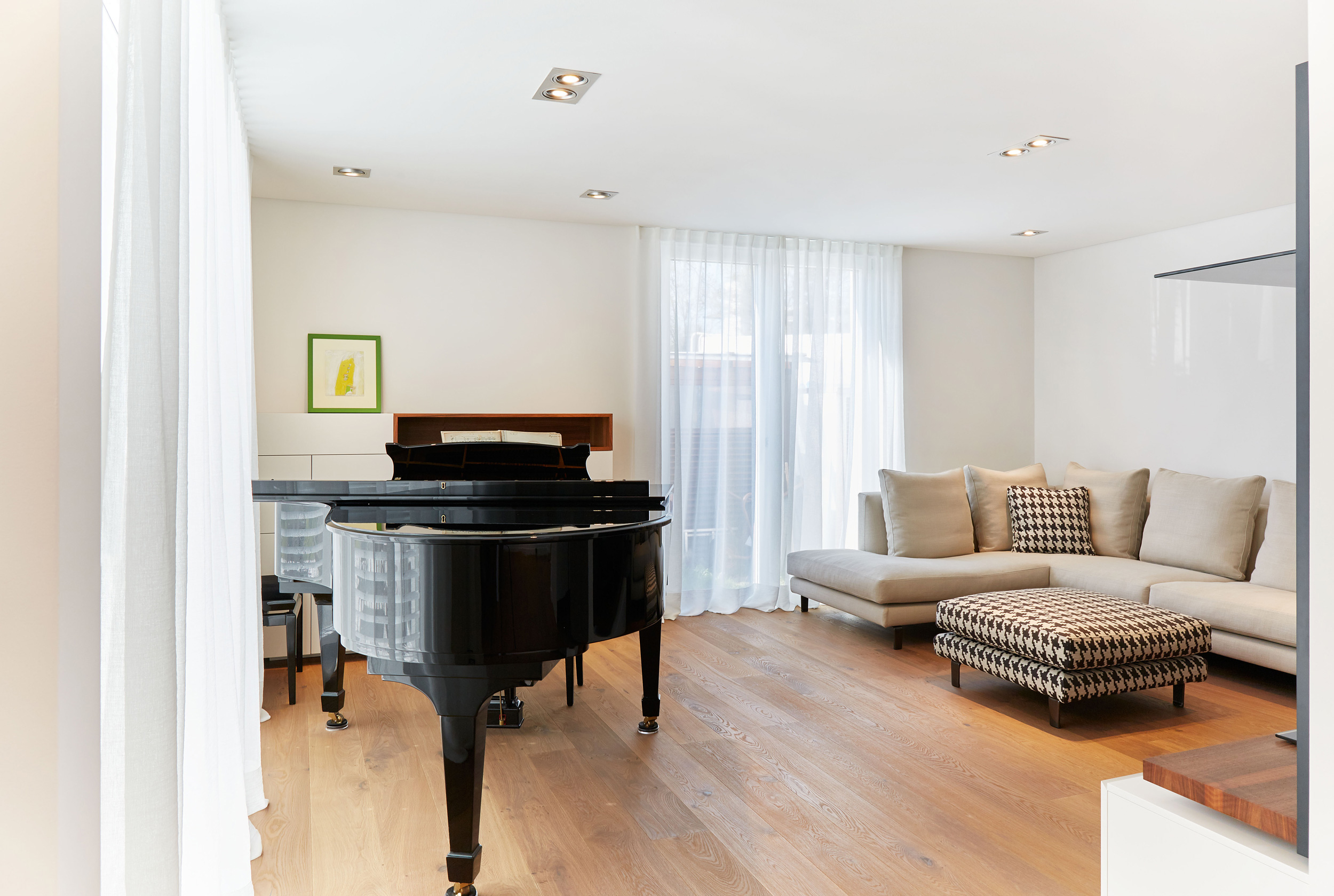 Foto: Heller, modern eingerichteter Wohnraum mit großem cremefarbenem Ecksofa, gemustertem Hocker, Holzboden und minimalistischen Regalen neben einem schwarzen Klavier.